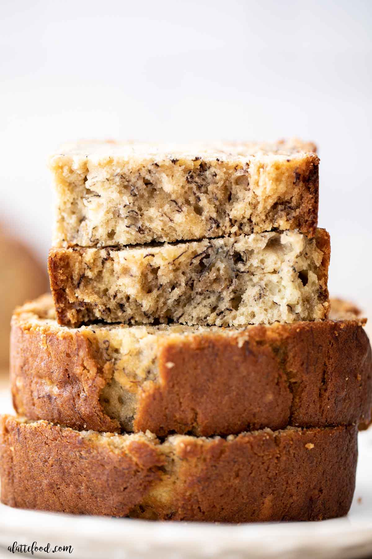 stack of banana bread slices with the top slice cut in half on a white plate.