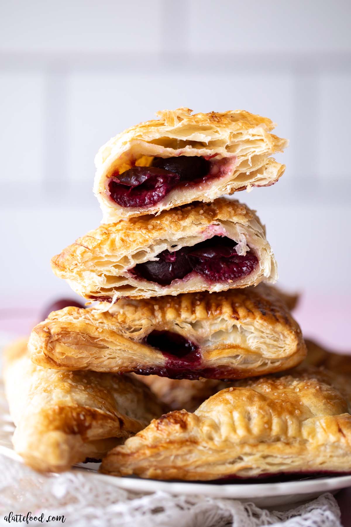 homemade cherry turnovers in puff pastry stacked on a white plate and cut in half.