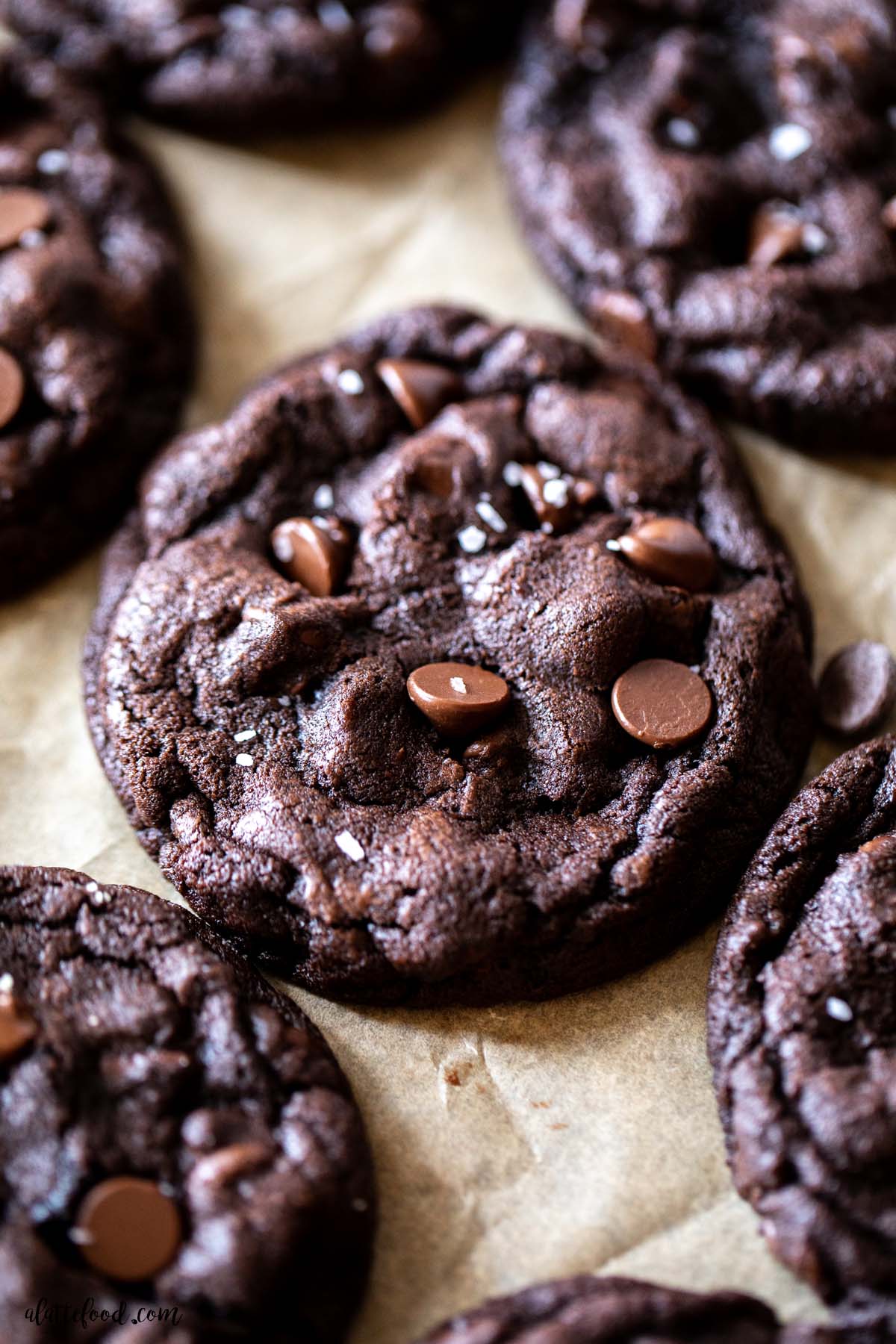 dark chocolate double chocolate chip cookies with sea salt on brown parchment paper.