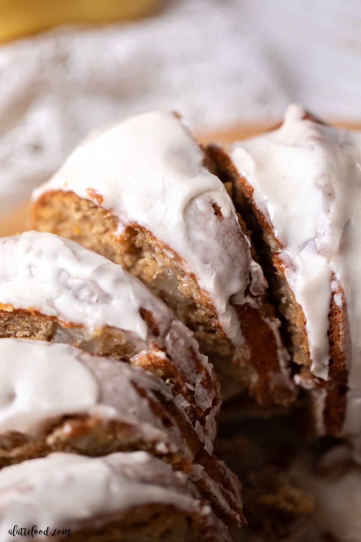 pear bundt cake with vanilla icing cut into slices on a wood cake stand.