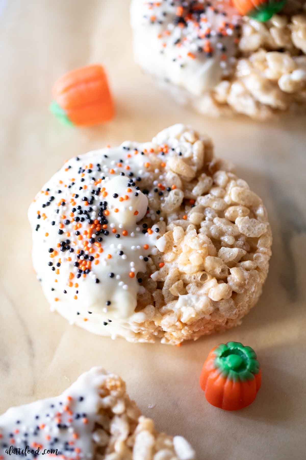 white chocolate pumpkin spice rice krispie treats cut into pumpkin shapes on brown parchment paper.